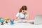 Dissatisfied tired little kid schoolgirl 12-13 years old study at white desk with pc laptop isolated on pink background