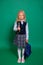 Dissatisfied, unhappy girl in a school uniform with a backpack and a book in her hands isolated on a green background