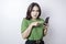 A dissatisfied young Asian woman looks disgruntled wearing green t-shirt irritated face expressions holding her phone