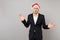 Dissatisfied young business man in classic suit, Christmas hat spreading hands isolated on grey background. Achievement