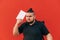 Dissatisfied young man in dark clothes and overweight stands on a red background with a book in hand and looks away