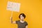 Dissatisfied young protesting girl hold protest sign broadsheet placard on stick isolated on yellow background studio