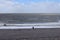 In the distance, a couple stand at the waters edge and watch the waves and the sea at Bossington Beach in Somerset, England