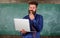 Distance education concept. Teacher bearded man with modern laptop surfing internet chalkboard background. Surfing