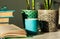 Distance home education: pile of books in colorful covers, glasses, cup of tea and Sansevieria snake plant in ceramic pots on a