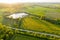 Distant Aerial View on Farmland with Rapeseed Fields and Pond on Sunny Spring Evening