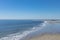 Distant beachcombers along a flat, sandy beach by the ocean, calm waters and blue sky