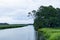 Distant boats moored in the waterway of a salt marsh, trees and distant treeline, early morning