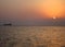 Distant crude oil taker on a sunset time against the sun in calm sea waters