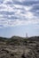 distant image of the Favaritx lighthouse, with a rock formation around it on a cloudy summer day, vertical, copy space