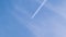 Distant passenger jet plane flying on high altitude on blue sky with white clouds leaving smoke trace of contrail behind