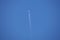 Distant passenger jet plane flying on high altitude on clear blue sky leaving white smoke trace of contrail behind. Air