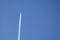 Distant passenger jet plane flying on high altitude on clear blue sky leaving white smoke trace of contrail behind. Air