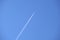 Distant passenger jet plane flying on high altitude on clear blue sky leaving white smoke trace of contrail behind. Air