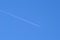 Distant passenger jet plane flying on high altitude on clear blue sky leaving white smoke trace of contrail behind. Air