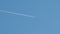 Distant passenger jet plane flying on high altitude on clear blue sky leaving white smoke trace of contrail behind. Air