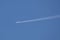 Distant passenger jet plane flying on high altitude on clear blue sky leaving white smoke trace of contrail behind. Air