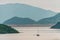 Distant sailboat floating on lake water on green mountains background. Scenic view of Plover Cove from Sha Lan villas at Shuen Wan