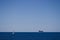 Distant Ship sailing across dark blue ocean towards small rocky island.