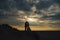 Distant view of marriage pair silhouette on evening beach. Dramatic sky with sun rays among clouds in background