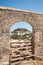 Distant view through stone arch opening at Lindos Town and Castle with ancient ruins of the Acropolis on sunny warm day. Island of