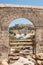 Distant view through stone arch opening at Lindos Town and Castle with ancient ruins of the Acropolis on sunny warm day. Island of