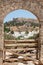 Distant view through stone arch opening at Lindos Town and Castle with ancient ruins of the Acropolis on sunny warm day. Island of