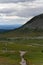 Distant view of unrecognizable hikers walking together on a path across green open plain and mountains