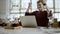 Distant view of a young businessman sitting at a table in a cafe using iphone and laughing, watching the passersby