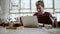 Distant view of a young businessman sitting at a table in a cafe using iphone and laughing, watching the passersby