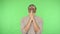 Distressed brunette man clasping hands in prayer, looking up with pleading expression. green background, chroma key