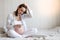 Distressed pregnant woman sitting on the bed holding a thermometer and holding his head. The concept of women`s health during