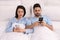 Distrustful young couple peering into each other`s smartphones in bed at home
