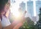 Diverse Asian girl looking at smart phone in urban city park with bright afternoon sunshine - Young millennial hipster