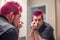 Diverse caucasian man with spiked pink hair applying eyeliner in the mirror