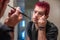 Diverse caucasian man with spiked pink hair applying eyeliner in the mirror