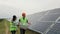 Diverse engineers talking and checking scheme plan while standing at solar energy farm. Woman and man in working clothes
