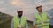 Diverse ethnicity male engineers communicating while walking at solar panels farm. Men in uniform and hard helmet