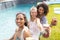 Diverse female friends are enjoying a sunny poolside gathering, holding refreshing drinks