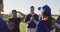 Diverse group of female baseball players and coach on pitch, clapping and high fiving