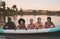 Diverse group of friends having fun while swimming at a lake in summer with a floating kayak boat. Happy, young and