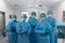 Diverse group of male and female surgeons standing in operating theatre wearing protective overalls