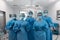 Diverse group of male and female surgeons standing in operating theatre wearing protective overalls