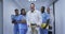 Diverse group of smiling male and female doctors in hospital corridor wearing scrubs and lab coats