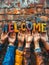 Diverse hands raised and holding colorful letters spelling Welcome against a rustic brick wall background, symbolizing unity