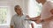 Diverse male physiotherapist with tablet shaking hands with senior male patient, in slow motion