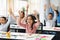 Diverse small schoolchildren raising hands at classroom