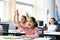 Diverse small schoolchildren raising hands at classroom