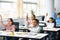 Diverse small schoolkids raising hands at classroom