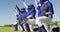 Diverse team of female baseball players in face masks kneeling in line with arms raised